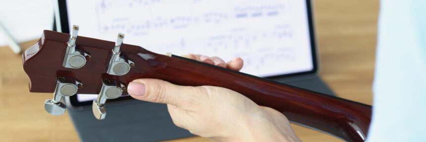 Gitara w kobiecych rękach na tle tabletu z zbliżeniem nut